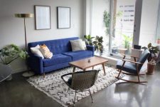 a chic and simple mid-century modern living room with a bold blue sofa, a woven chair, a printed rug and pillows and statement plants
