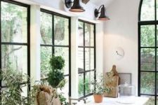 a chic farmhouse kitchen with black French windows, neutral wooden cabinets, black sconces, wooden beams on the ceiling and greenery