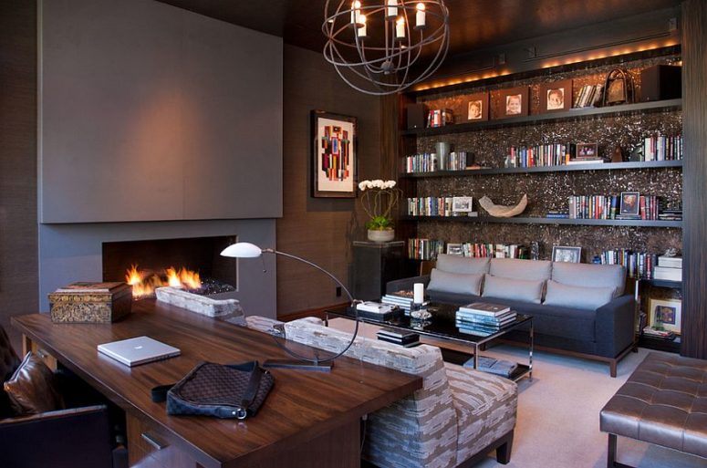 a chic home office with grey walls and a built-in fireplace, built-in shelves, grey seating furniture, a glass coffee table, a stained desk and leather chairs