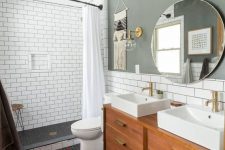 a chic mid-century modern bathroom with a grey accent wallpenny and subway tiles, a stained vanity, a round mirror and two sinks