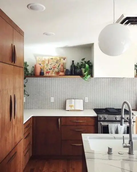 a chic mid-century modern kitchen with dark stained cabinets and white ones, white stone countertops and a white tile backsplash and lights and lamps