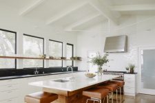 a chic mid-century modern kitchen with white cabinets, black countertops and a backsplash, a wooden kitchen island and leather stools
