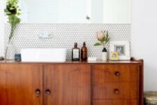 a chic mid-century modern space with white hex tiles and black usual ones, a rich stained vanity and a statement mirror