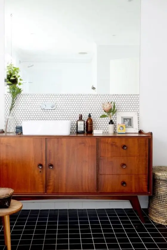 A chic mid century modern space with white hex tiles and black usual ones, a rich stained vanity and a statement mirror