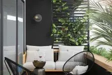 a chic modern balcony done in black and white, with a neutral stained sofa, black chairs, a black round table and lots of greneery