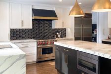 a chic modern kitchen with white shaker style cabinets, white stone countertops, a black hex tile backsplash, gold pendant lamps and chrome finish appliances