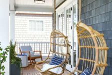 a coastal porch with a wooden deck, rattan hanging chairs with printed pillows, a rocker with a side table and lots of greenery