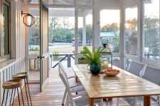 a coastal screened porch with a pass by window, a wooden dining table and white chairs plus views of the surroundings
