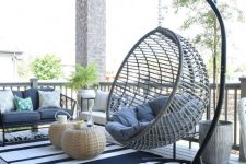 a coastal terrace with a wooden deck, rattan furniture, printed and neutral textiles, a hanging chair on a stand and wicker side tables