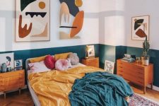 a colorful mid-cenntury modern bedroom with white and teal color block walls, an upholstered bed, stained furniture, colorful bedding and colorful artworks