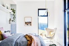 a colorful mid-century modern bedroom with a view, a bed with colorful bedding and a printed rug, potted greenery and a chic chandelier