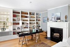 a cool and light-filled home office with built-in shelves, a fireplace, a black desk, a white sofa, some decor is very cool