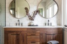 a cool mid-century modern bathroom with white hex tiles, a stained vanity, round mirrors, pendant lamps, a striped rug