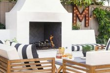 a cool modern terrace with a white fireplace, light stained furniture, black and white textiles, potted greenery and a marquee letter is amazing