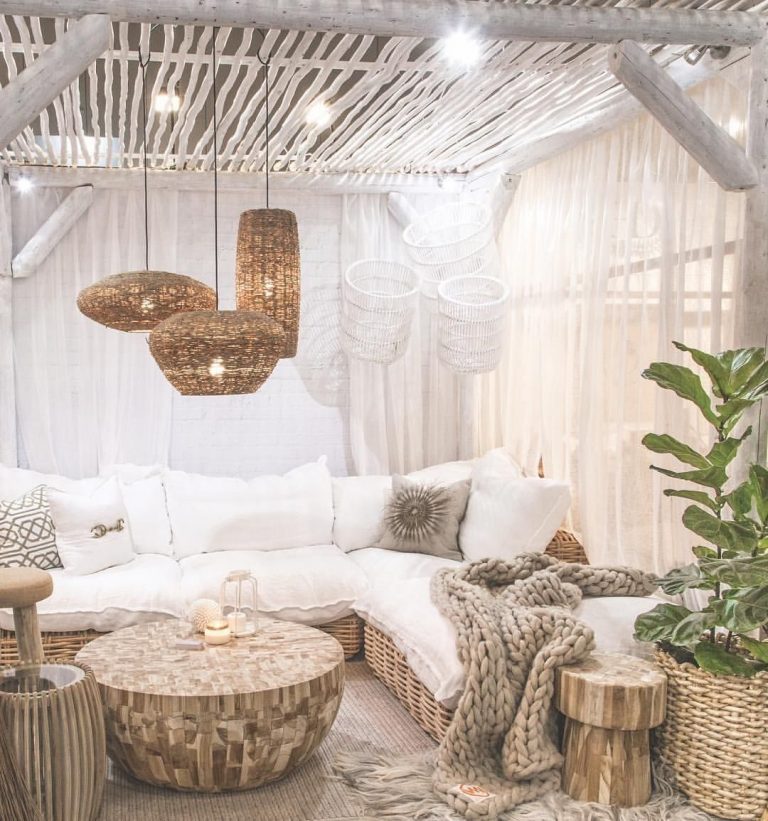 a cozy boho pergola with pendant lamps and lights, a woven corner sofa, wooden stools and a coffee table plus neutral upholstery is wow