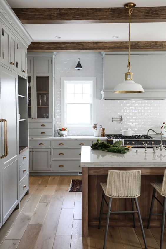 a cozy farmhouse kitchen with dove grey cabinets, brass handles and knobs and a pendant gold and white lamp - pairing gold and brass is always a good idea