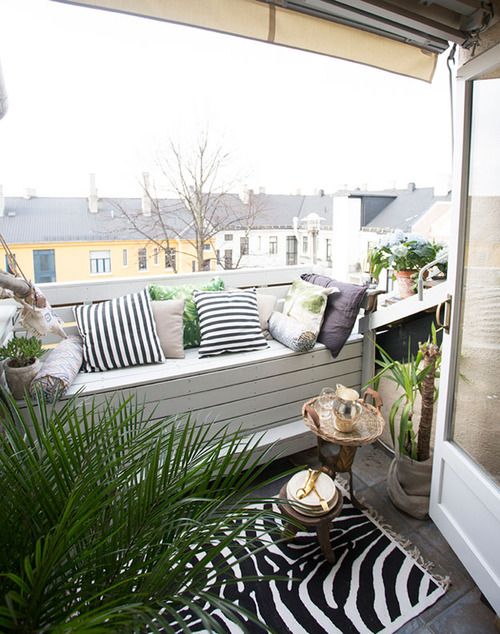 a cozy modern balcony with a white pallet bench, printed textiles, some greenery and blooms and a view of the roofs is a lovely space
