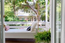 a cozy small porch with a white daybed hanging here and bright pillows plus a potted fern is a cool space to be