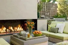 a cozy terrace with a fireplace, simple contemporary furniture with green upholstery, touches of orange for a stronger summer feel