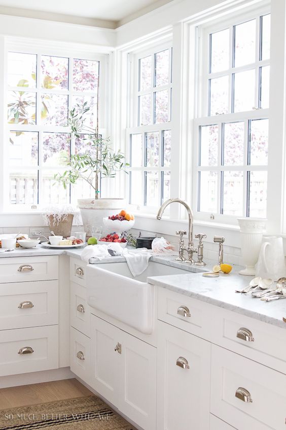 a cozy white farmhouse kitchen with shaker style cabinets, a corner French window that provides lovely views of the garden