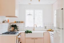 a cute pink mid-century modern kitchen with white square tile backsplash, white countertops and glam gold fixtures