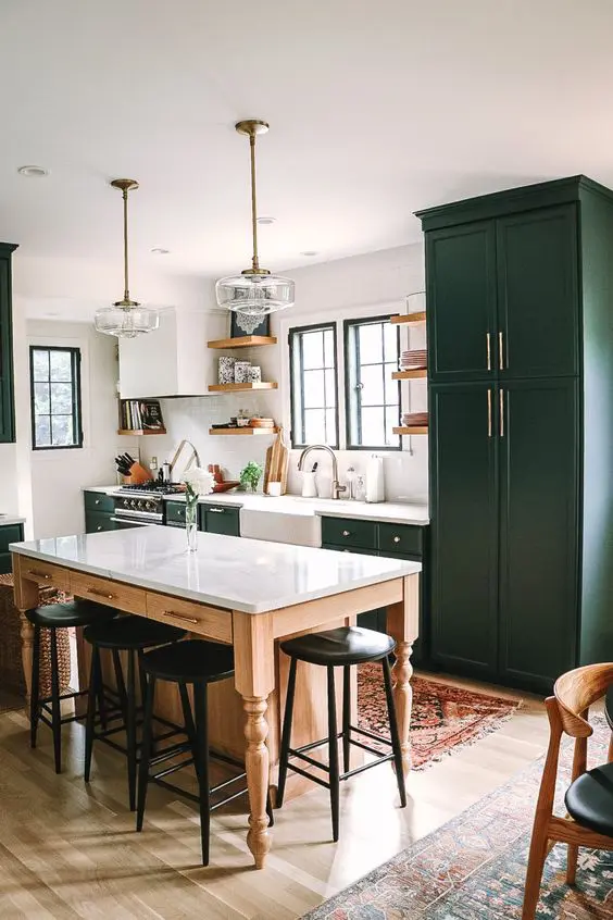 a dark green mid-century modern kitchen with shaker style cabinets, white stone countertops, a table kitchen island and black stools