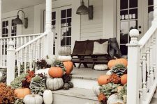 a farmhouse porch with a dark stained bench and pillows, lots of bright blooms and pumpkins on the steps is a cool idea