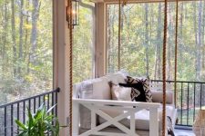 a farmhouse porch with a white hanging bed and printed pillows, potted plants and a candle lantern is a lovely idea to rock