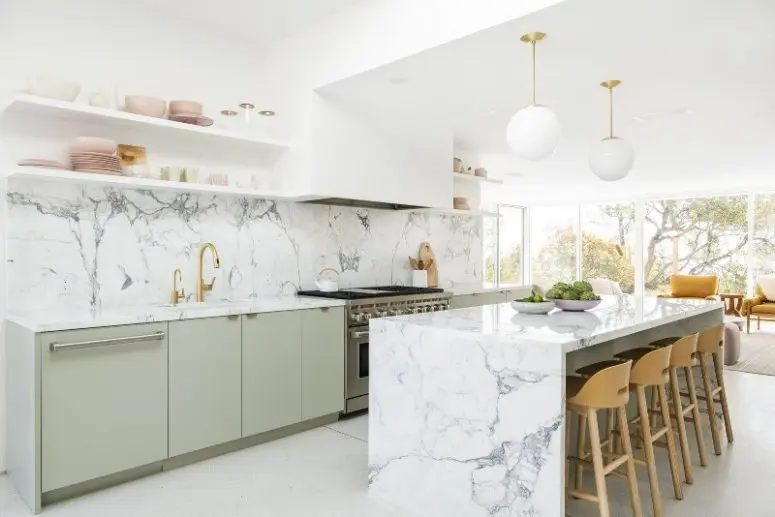 a glam mid-century modern kitchen with green cabinets, open shelves, a white hood, shelves and a marble kitchen island