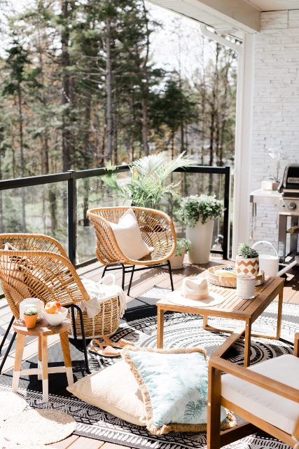 a gorgeous boho balcony with rattan and wooden furniture, printed rugs and pillows, potted greenery and a cool forest view