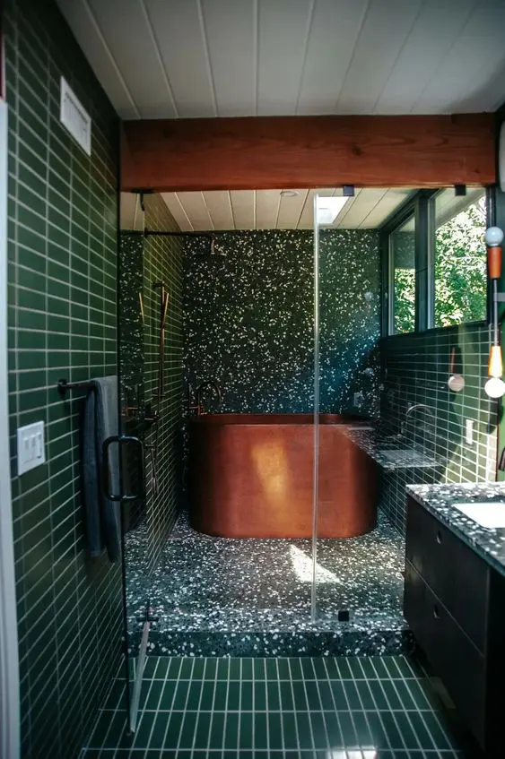 A green mid century modern bathroom with terrazzo and skinny tiles, windows, a copper soak tub, a floating vanity