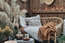 a hippie style outdoor space with a rattan sofa, pampas grass, a metal table and candle lanterns, woven decorative plates