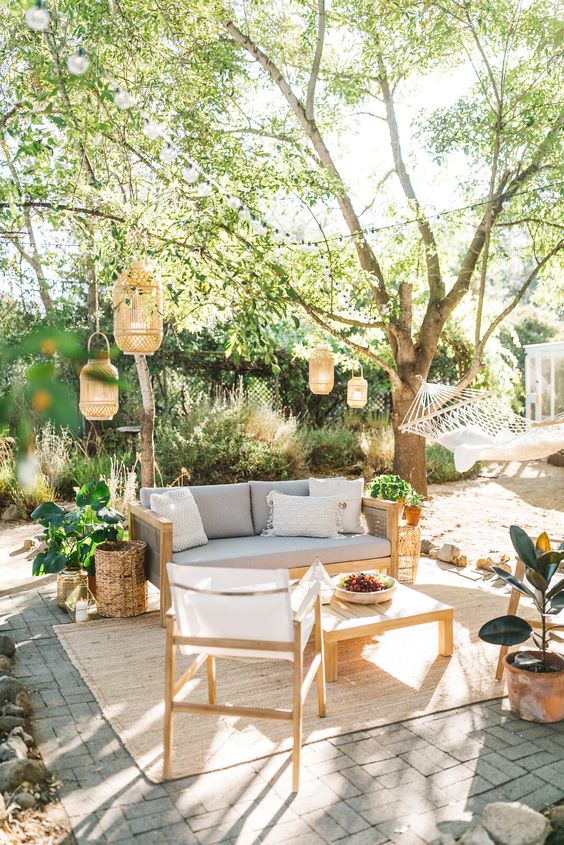 a light filled outdoor space with wooden furniture, neutral upholstery, candle lanterns and statemrnt plants around welcomes