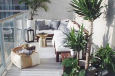 a lovely and welcoming balcony with a rich-stained wooden bench with white upholstery, potted plants, a small pouf and a striped rug