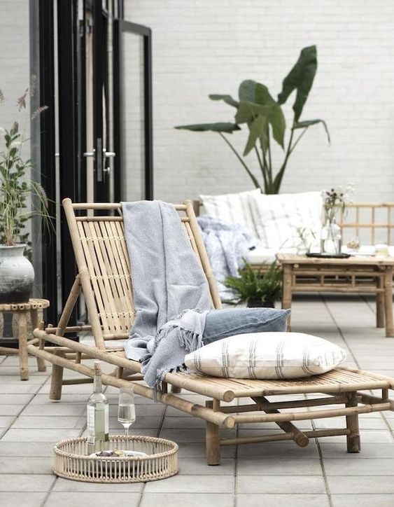 a lovely bamboo lounger with neutral and pastel pillows, a matching stool and a tray for a relaxed tropical outdoor space