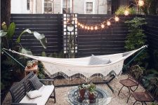 a lovely boho space with lots of greenery, a beautiful hammock, vintage garden furniture, a glass coffee table and string lights