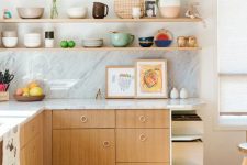 a lovely mid-century modern kitchen with light-stained cabinets, a white stone countertop and a backsplash, open shelves