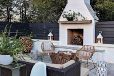 a lovely modern terrace with a white brick fireplace, rattan and wicker furniture, potted greenery, firewood and pretty side tables