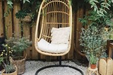 a lovely outdoor nook just for one, with a hanging chair on a stand and lots of potted greenery and blooms