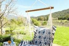 a lovely outdoor nook with a cool view, a floral side table, a cool hanging chair with cushions and pillows is a very welcoming idea