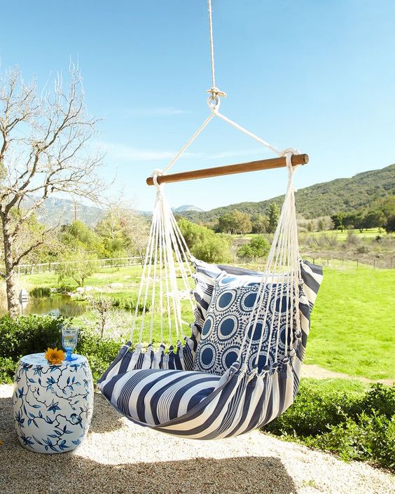 a lovely outdoor nook with a cool view, a floral side table, a cool hanging chair with cushions and pillows is a very welcoming idea