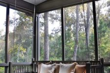 a lovely screened porch with a birck floor, a hanging black bench, a small folding table and gorgeous views of the forest around