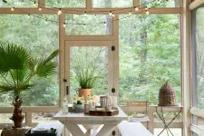 a lovely screened porch with a white trestle table, shabby chic benches, side tables, potted plants and some string lights