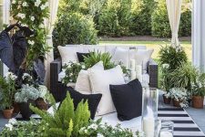 a lovely terrace with black wicker furniture, a stone coffee table, lots of potted greenery and blooms hanging and standing around