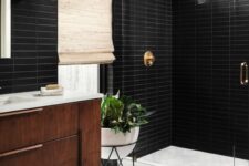 a mid-century modern bathroom with black skinny and white hex tiles, a stained vanity, a shower space, brass fixtures and potted plants