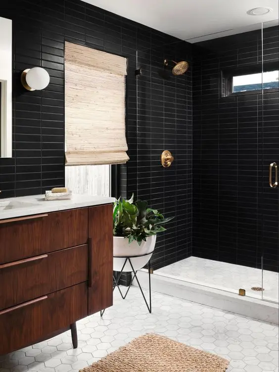 A mid century modern bathroom with black skinny and white hex tiles, a stained vanity, a shower space, brass fixtures and potted plants