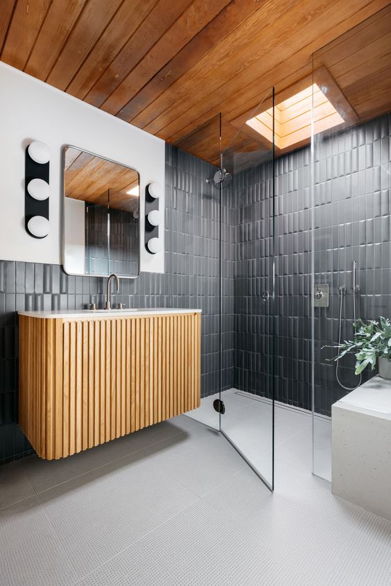A mid century modern bathroom with graphite grey tiles, a fluted floating vanity, a shower space with a skylight