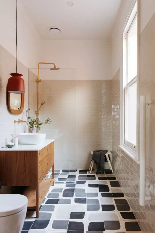 a mid-century modern bathroom with grey and graphic black and white tiles, a stained vanity, white appliances and gold fixtures