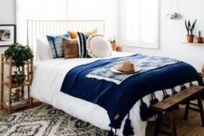 a mid-century modern boho bedroom with a metal bed, wooden nightstands, a wooden bench, printed pillows and a rug