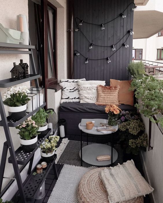 a modern Scandinavian balcony with a black accent wall, a black built-in bench, pretty pillows, potted plants, a jute pouf and a pillow